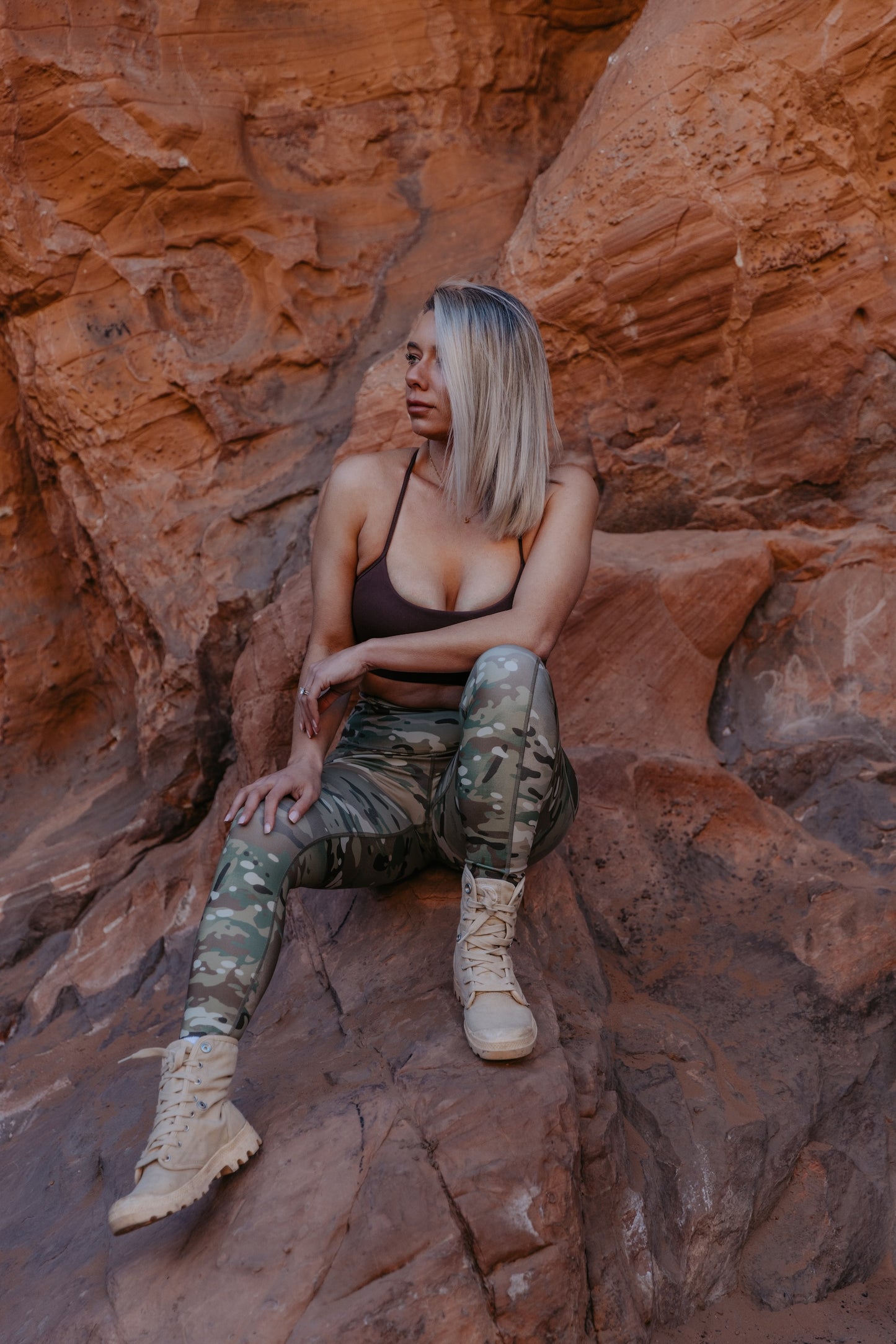 Women’s camo leggings in MULTICAM® print styled outdoors on red rock terrain with sports bra and boots