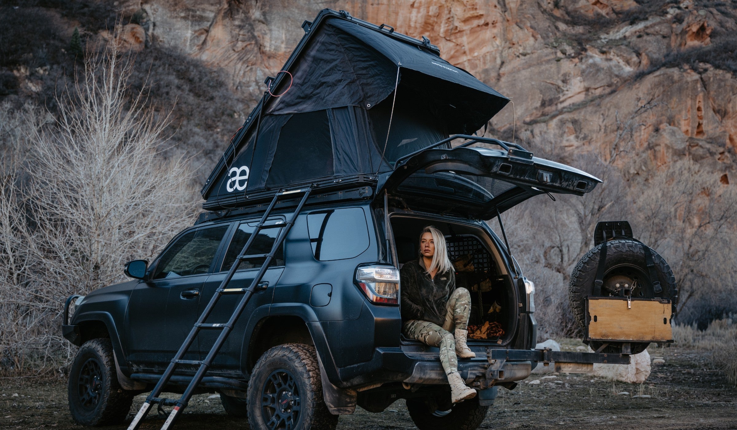 Woman wearing Fit By Nature MULTICAM Leggings sitting on SUV in rugged outdoor desert setting