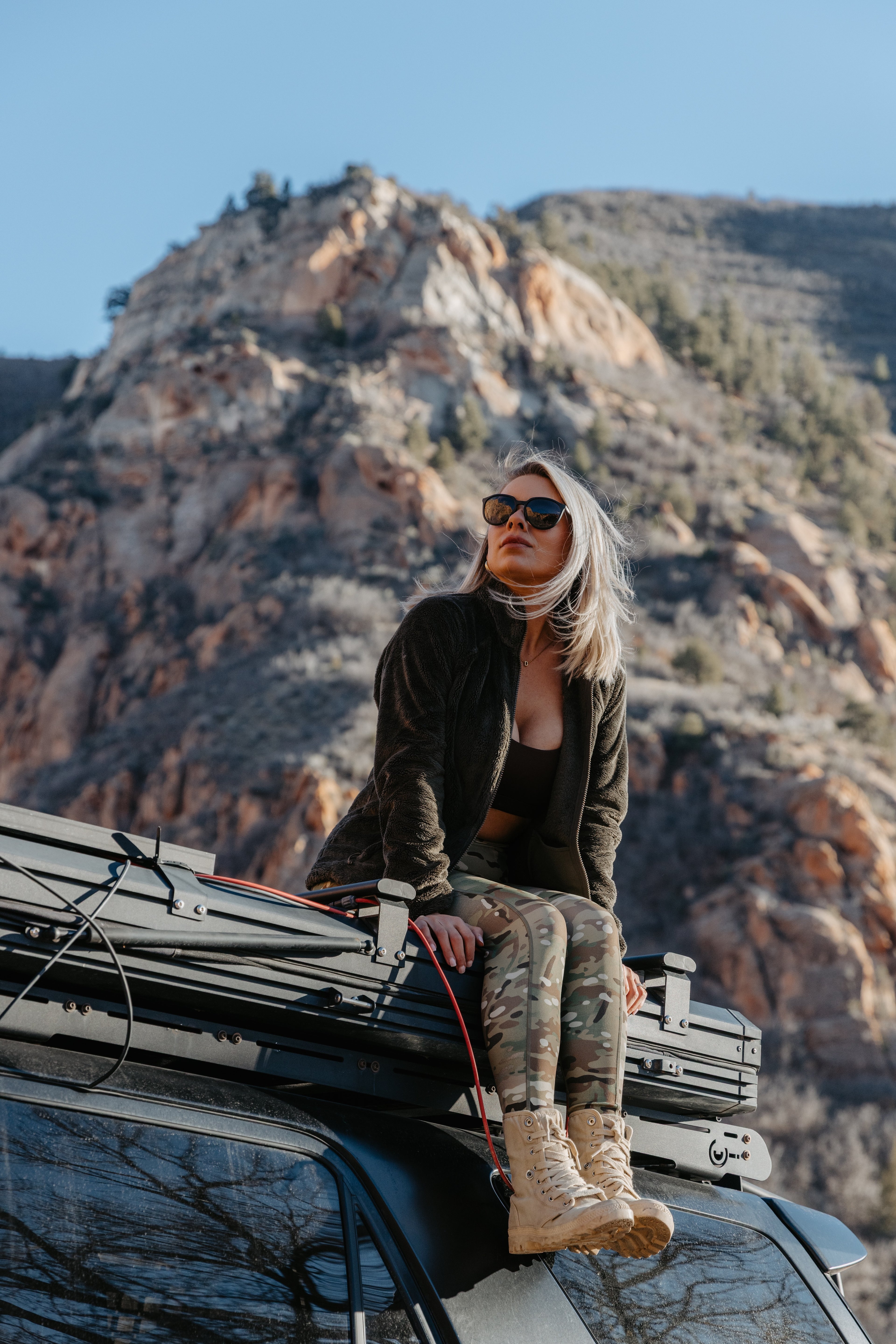 Active woman in MULTICAM performance leggings sitting on overland vehicle in rocky desert setting